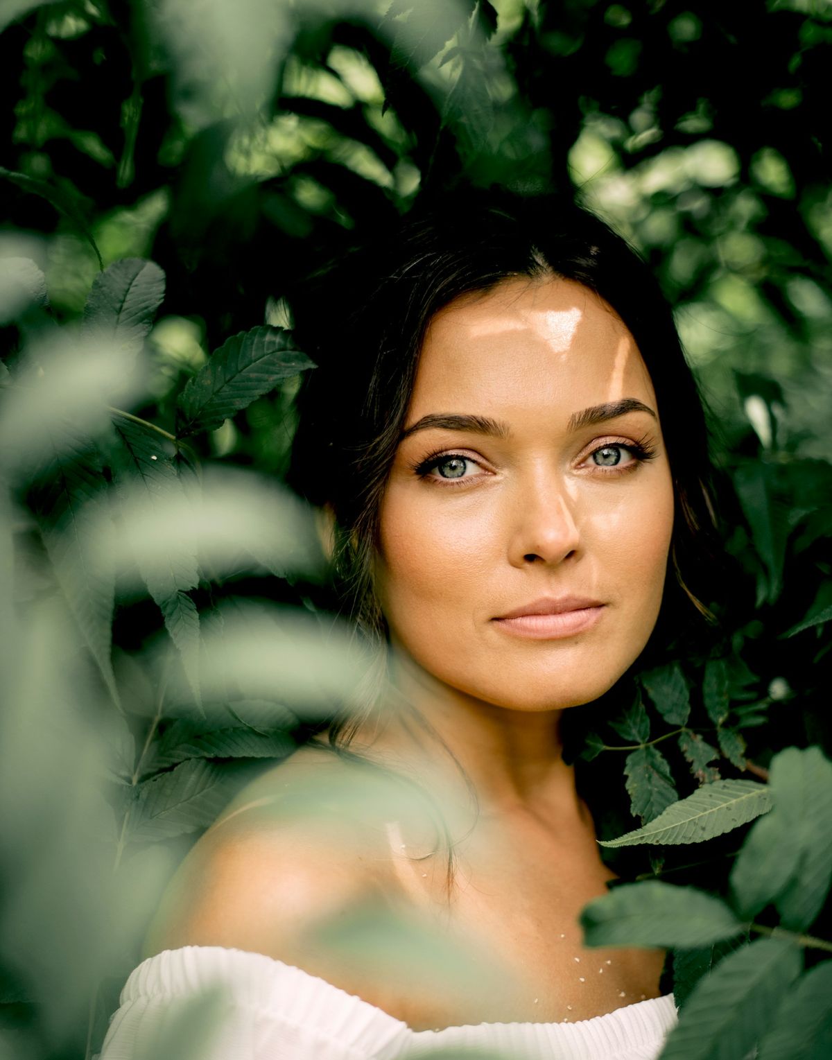 Rosto de mulher entre folhagem verde, em luz natural